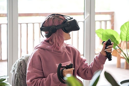 Jugendliche spielt mit VR-Brille und Controllern
