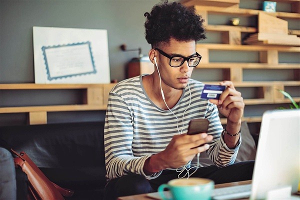 Junger Mann tippt für das Online-Shopping seine Kreditkarteninformationen ins Handy ein.
