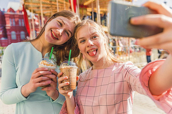 Zwei Mädchen machen ein Selfie von sich auf einem Jahrmarkt.