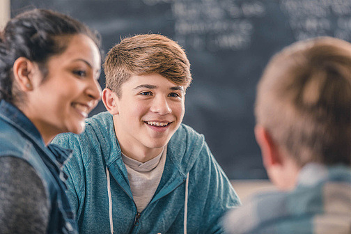Drei Jugendliche sitzen im Klassenzimmer vor einem Laptop und diskutieren. 