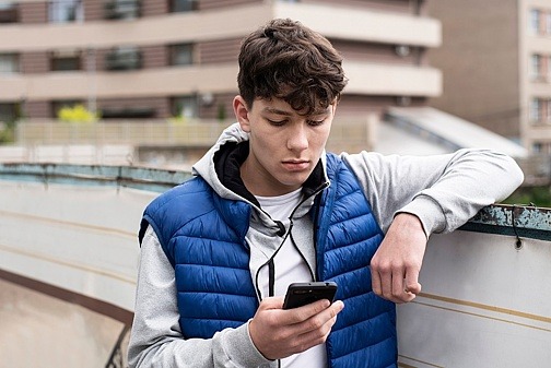 Teenager lehnt an Mauer mit Blick auf Smartphone