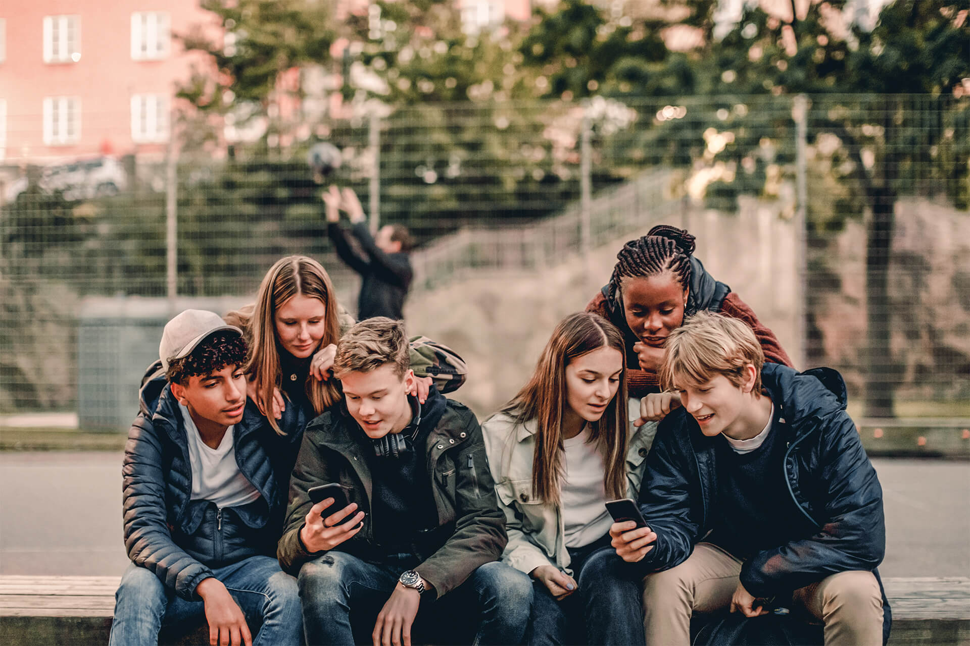 Sechs Jugendliche sitzen im Park und nutzen zwei Smartphones. 