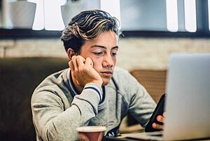 Junge sitzt vor dem Laptop, whärend er gleichzeitig sein Smartphone nutzt.