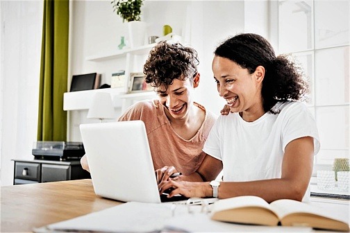 Mutter und Sohn sitzen am Laptop und lachen gemeinsam.