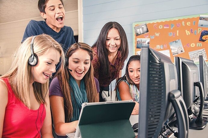 Eine Gruppe Jugendlicher sitzt vor einem Tablet mit Headsets.