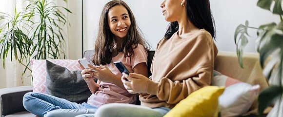 Mutter und Tochte mit Smartphones auf Sofa