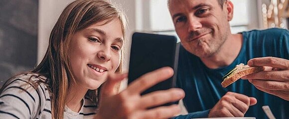 Tochter zeigt Vater etwas auf Smartphone