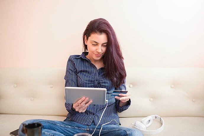 Jugendliche sitzt mit Tablet und Kreditkarte auf Couch