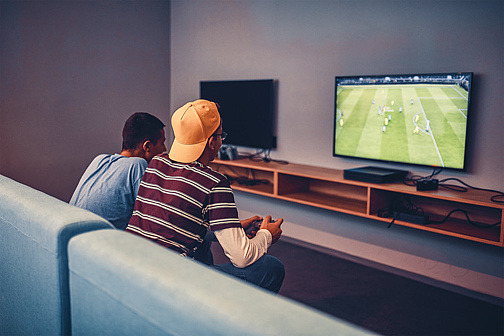 Zwei Jungen sitzen auf Sofa und spielen Videospiel gegeneinander