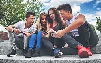 Gruppe Jugendliche sitzen draußen und nutzen Smartphones