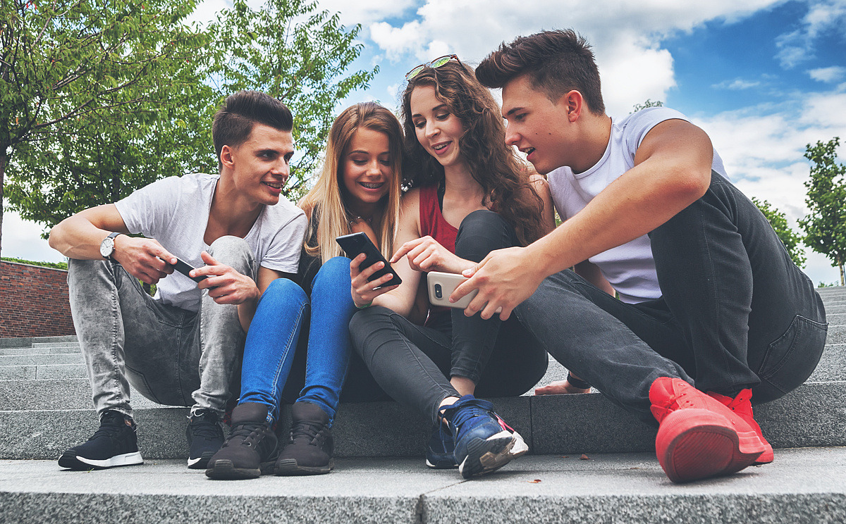 Gruppe Jugendliche sitzen draußen und nutzen Smartphones