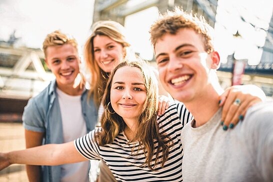 Vier Jugendliche stehen vor der Tower-Bridge in London und lachen in die Kamera..