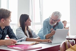 Lehrer erklärt Schülerin und Schüler etwas am Laptop