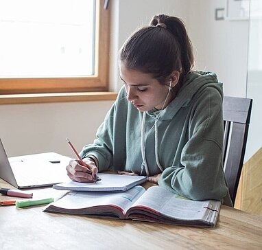 Schülerin arbeitet am Schreibtisch mit Laptop und Buch