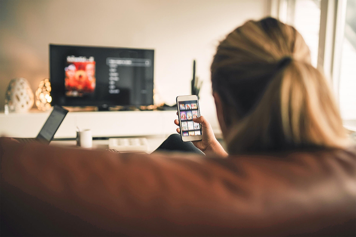 Mädchen schaut TV und sucht auf Smartphone Filme