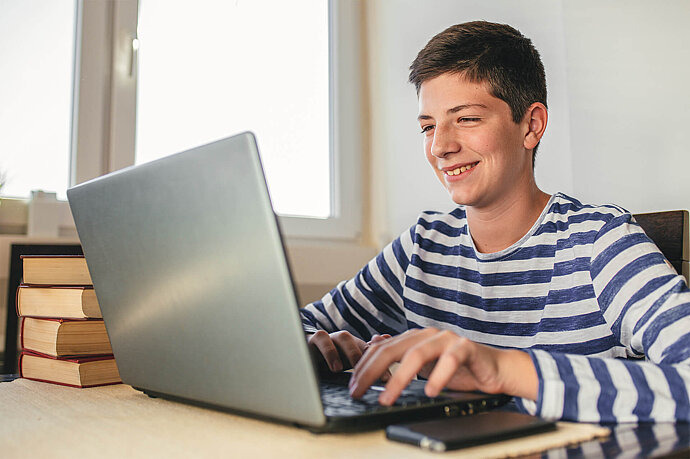 Junge sitzt am Tisch und tippt auf einem Laptop.