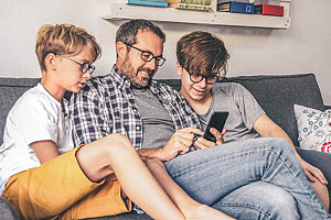 Vater mit Söhnen mit Smartphone, während er zu Hause auf dem Sofa sitzt