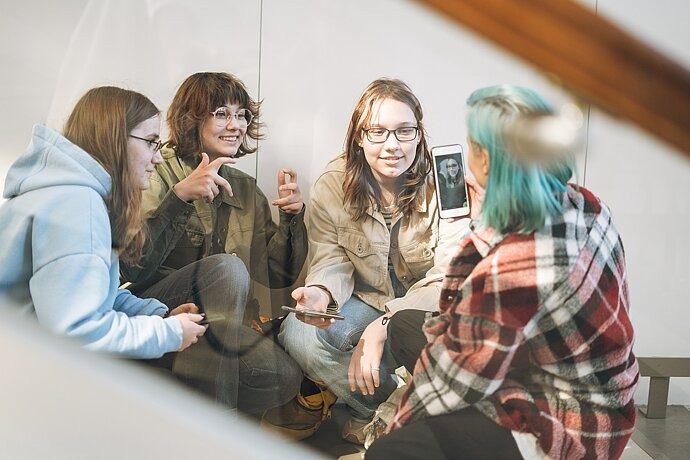 Vier Jugendliche reden lachend miteinander, eine Person filmt dabei eine andere.