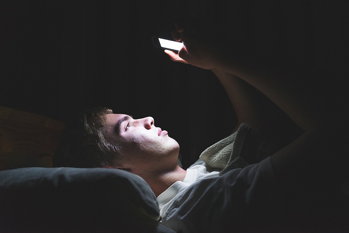 Junge im Dunkeln mit Smartphone im Bett