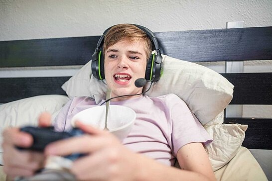 Junge liegt im Bett mit einem Headset und spielt ein Videospiel.