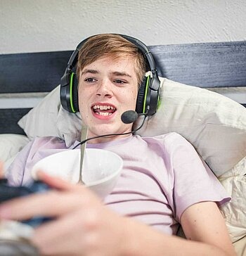 Junge liegt im Bett mit einem Headset und spielt ein Videospiel.