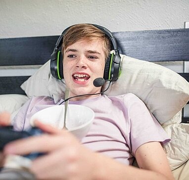Junge liegt im Bett mit einem Headset und spielt ein Videospiel.