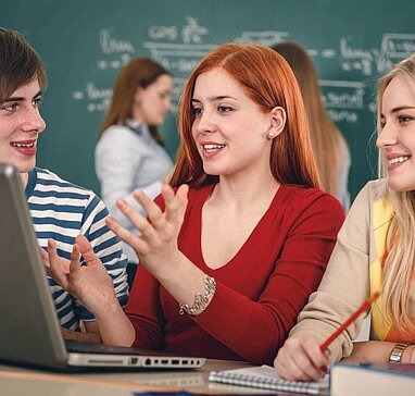 Drei Jugendliche im Klassenzimmer an Laptop 