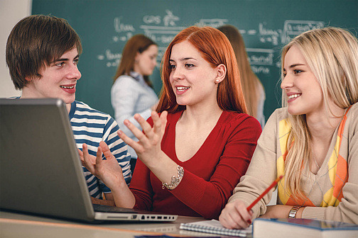 Drei Jugendliche im Klassenzimmer an Laptop 