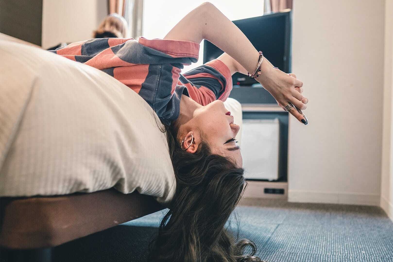 Jugendliche liegt rückwärts auf Bett und schaut aufs Smartphone