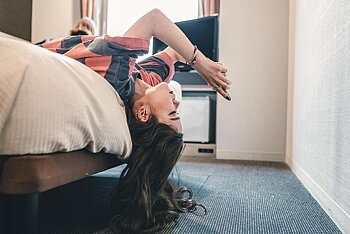 Jugendliche liegt rückwärts auf Bett und schaut aufs Smartphone