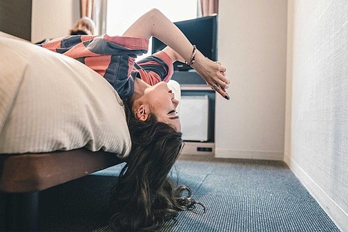 Jugendliche lässt Kopf vom Bett hängen und schaut aufs Smartphone.