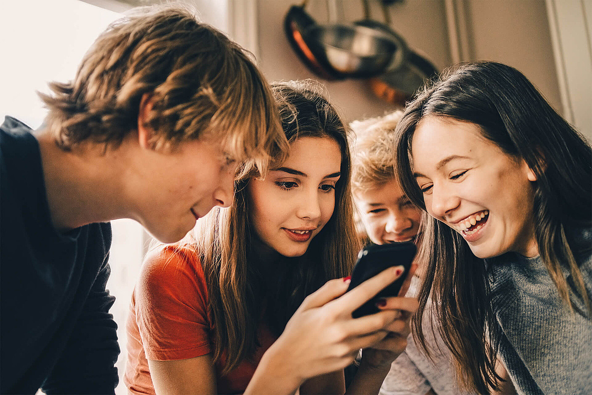 Eine Gruppe Jugendlicher schaut gemeinsam auf ein Handy und lachen dabei. 