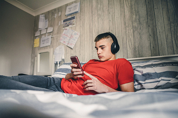 Jugendlicher liegt auf dem Bett mit dem Smartphone in der Hand.