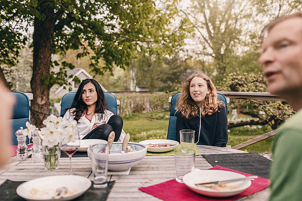Schwestern im Teenageralter sitzen mit ihrem Vater am gedeckten Tisch im Garten.