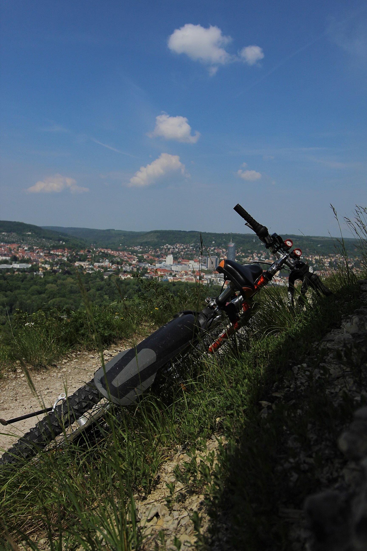 Fahrrad liegt gelehnt neben einem Hügel. Im Hintergrund ist eine Stadt zu erkennen.