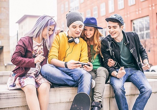 5 Jugendliche auf Mauer schauen auf Smartphone