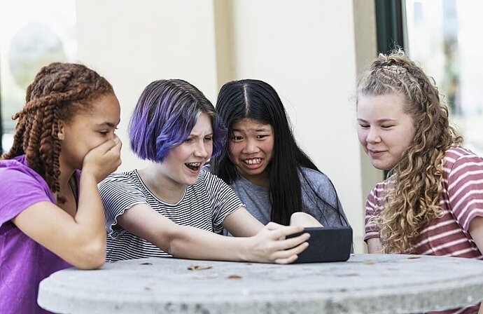 vier Jugendliche schauen geschockt auf Smartphone