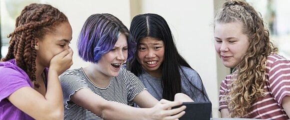 vier Jugendliche schauen geschockt auf Smartphone