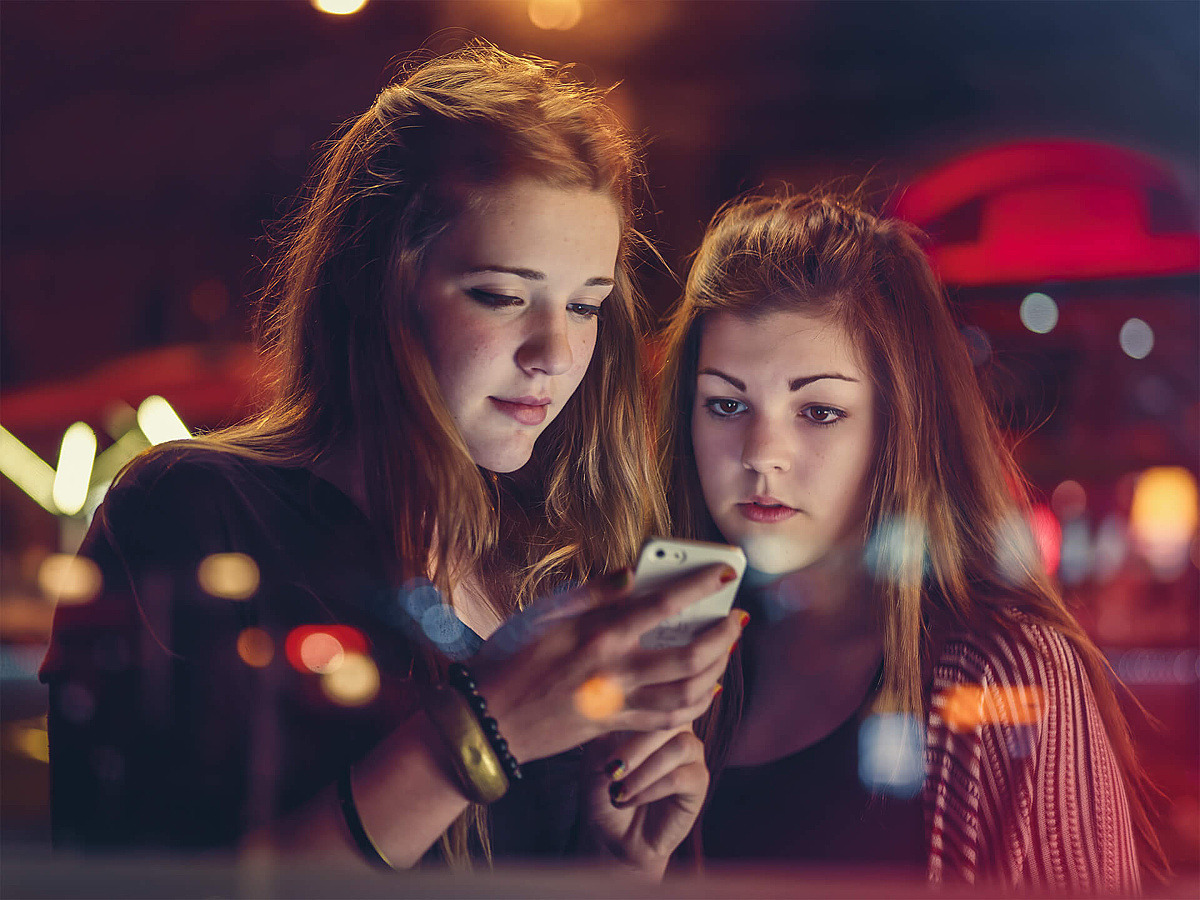 Zwei Mädchen schauen bei Nacht auf ein Handy. 