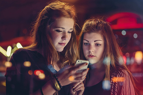 Zwei Mädchen schauen bei Nacht auf ein Handy. 