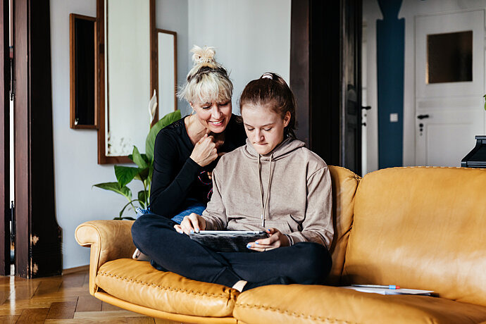 Mutter und Tochter sitzen auf dem Sofa und blicken auf das Tablet