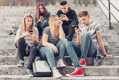 Mädchen sitzt gelangweilt in einer Gruppe, während die anderen alle aufs Handy schauen.
