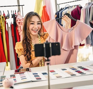 Influencerin filmt sich und hält Oberteil in Smartphone-Kamera
