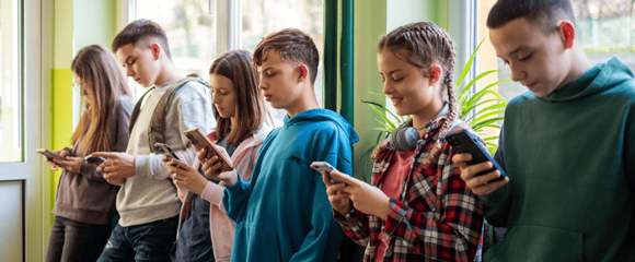 Teenager in Schule lehnen an Wand und schauen auf ihre Handys.