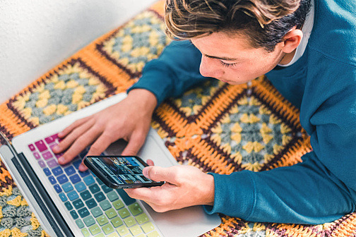 Teenager tippt auf Laptop und Smartphone gleichzeitig