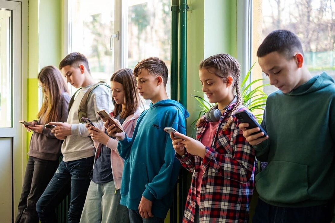 Teenager in Schule lehnen an Wand und schauen auf ihre Handys.