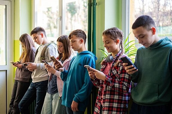 Teenager in Schule lehnen an Wand und schauen auf ihre Handys.