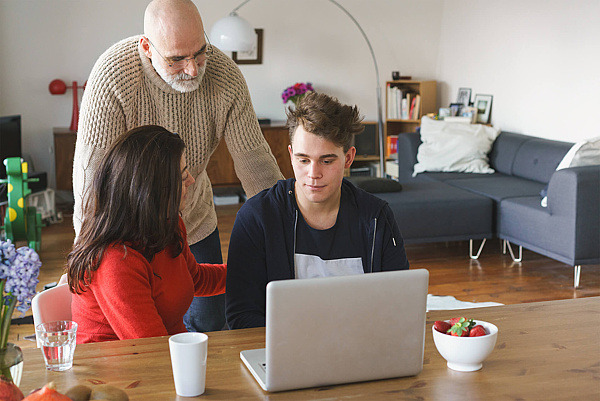 Eltern reden im Wohnzimmer vor einem Laptop mit ihrem jugendlichen Sohn über die Mediennutzung.