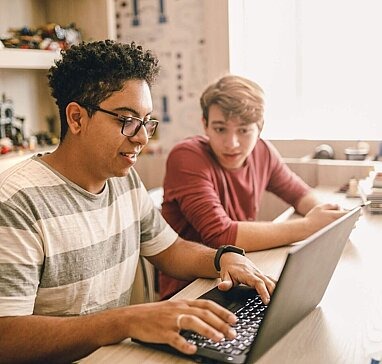Zwei Teenager arbeiten an einem Laptop.