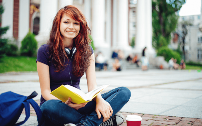 Mädchen sitzt mit Buch vor Bibliothek